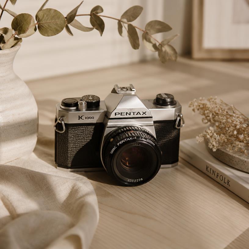 A vintage film camera on a wooden table with dried eucalyptus and soft shadows